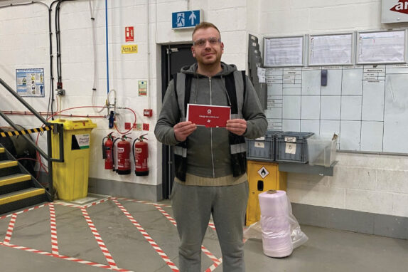 employee of the month Dmitrijs in the factory with a red gift envelope.