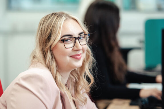 keira oddy, the customer support specialist, sat at her desk with blonder hair and a pink blazer on.